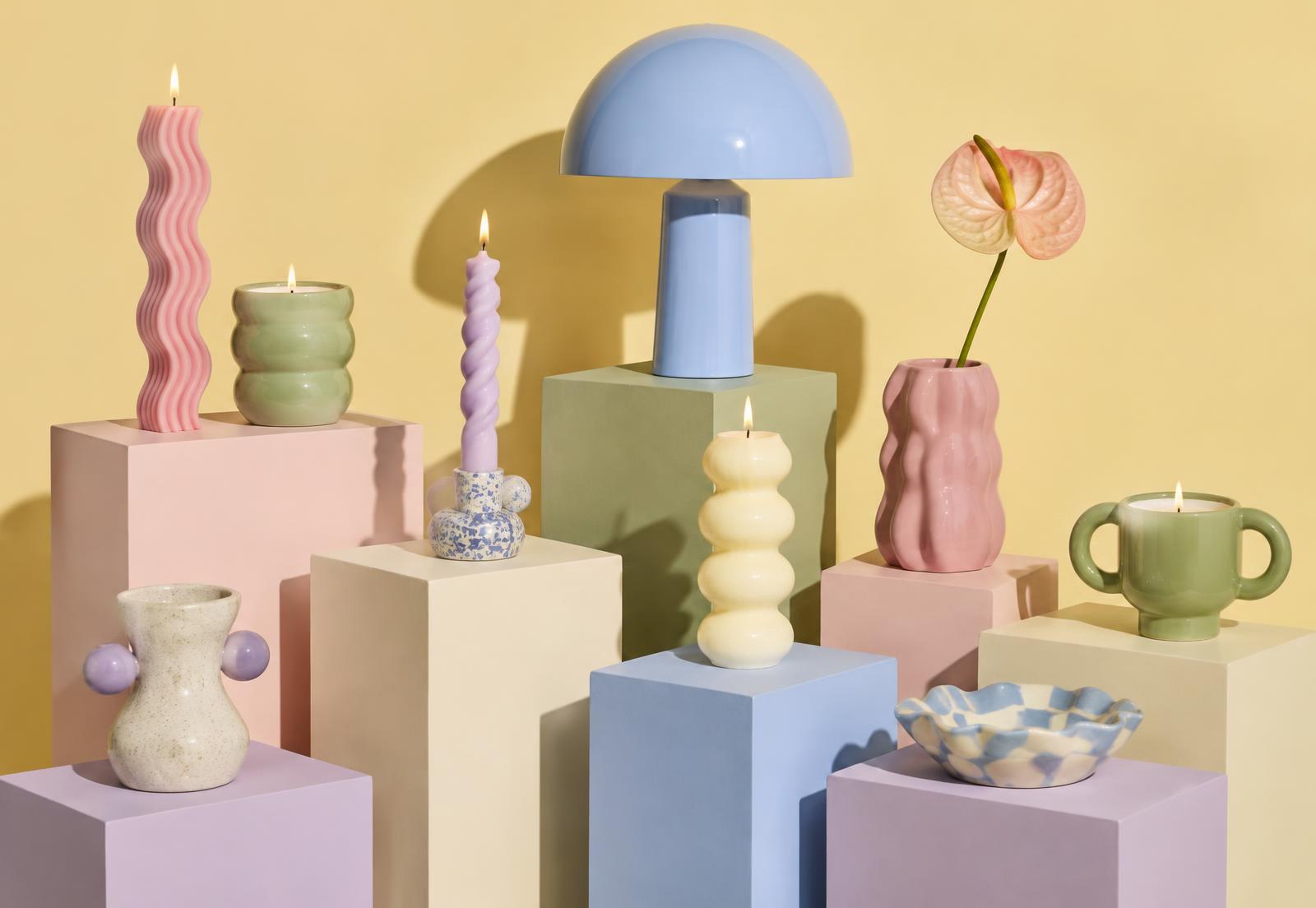 Pastel candles, a mushroom lamp and ceramic vessels arranged on colorful plinths